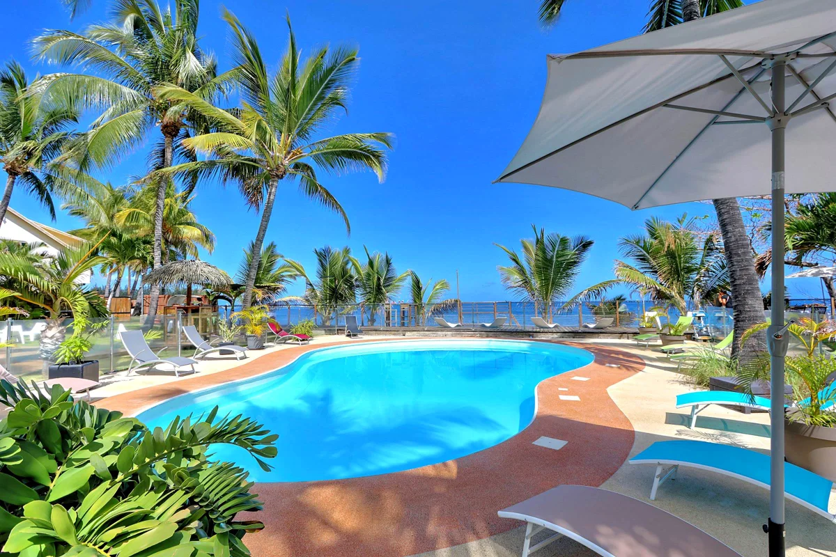 La piscine chauffée, ses transats et la mer derrière les cocotiers